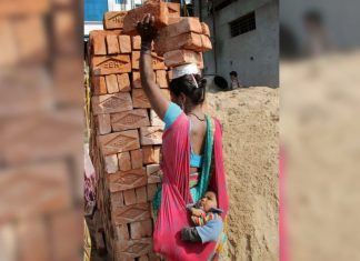 Mãe trabalha carregando tijolos na cabeça com o filho no colo