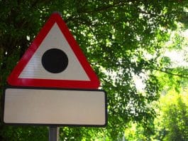 Placa de trânsito com triângulo vermelho e um ponto preto no centro